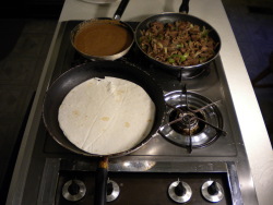 Here is the Mexican Burrito recipe being prepared on the stove, with a frying pan full of the meat and onion mixture, a frying pan of refried beans, and a special burrito tortilla being heated.